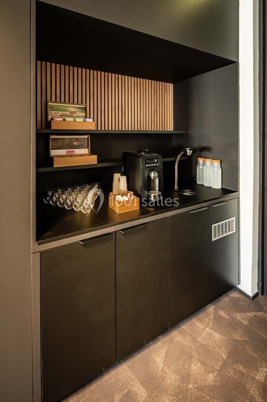 Coin café avec machine à café, verres, bouteilles d'eau et étagères en bois dans un espace au design moderne.