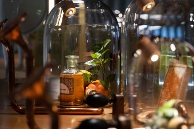 Flacons et éléments décoratifs sous cloches en verre sur une table éclairée dans un espace moderne et tamisé.