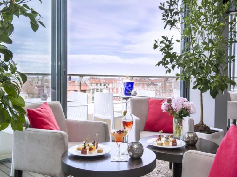 Salon lumineux avec vue sur la ville, tables garnies de desserts, cocktails et décorations florales.