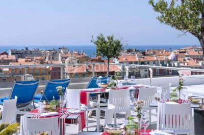 Miniature Location salle Nice (Alpes-Maritimes) - Aston La Scala Nice #10 Tables dressées avec chandelles et fleurs sur une terrasse offrant une vue nocturne sur des bâtiments éclairés.