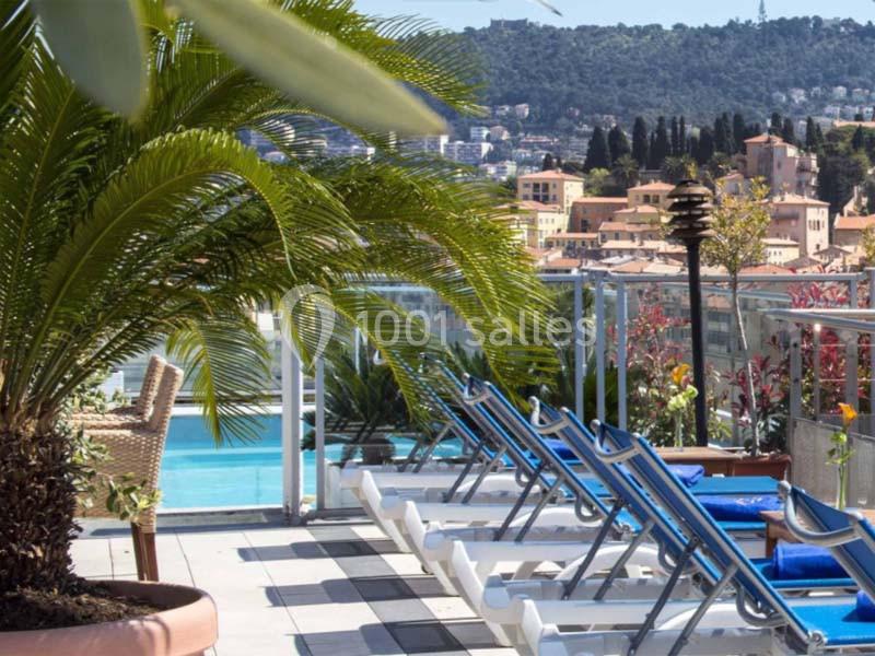 Chaises longues alignées près d'une piscine avec vue sur des collines et des bâtiments en arrière-plan.