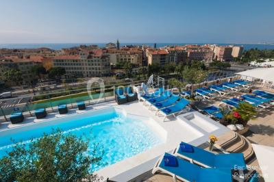 Miniature Location salle Nice (Alpes-Maritimes) - Aston La Scala Nice #3 Tables dressées avec chandelles et fleurs sur une terrasse offrant une vue nocturne sur des bâtiments éclairés.