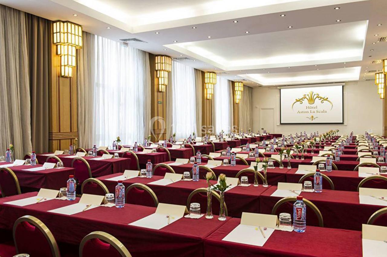 Salle de conférence aménagée avec des tables rouges, des chaises alignées et un écran de projection à l'arrière.