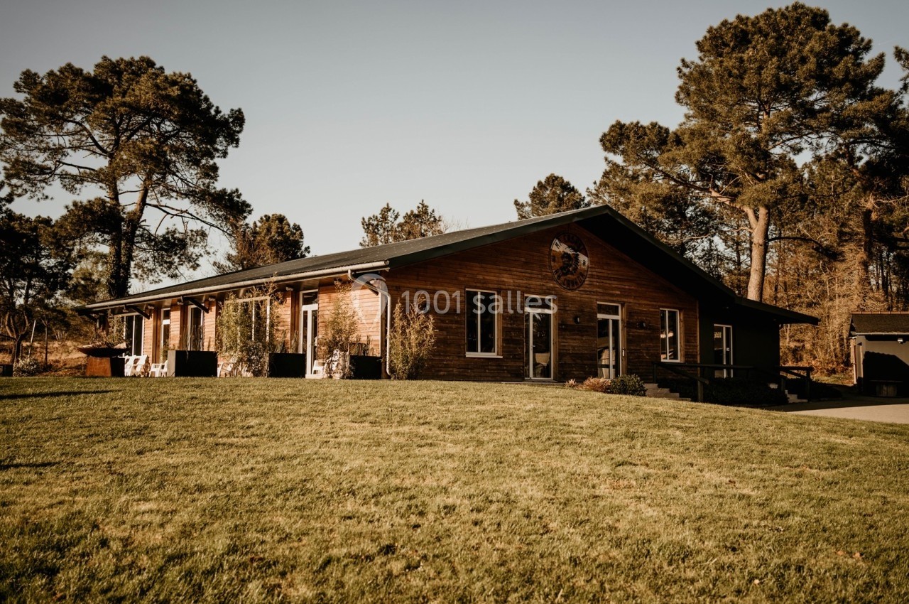 Bâtiment en bois de plain-pied entouré d'arbres, avec une pelouse verdoyante au premier plan.