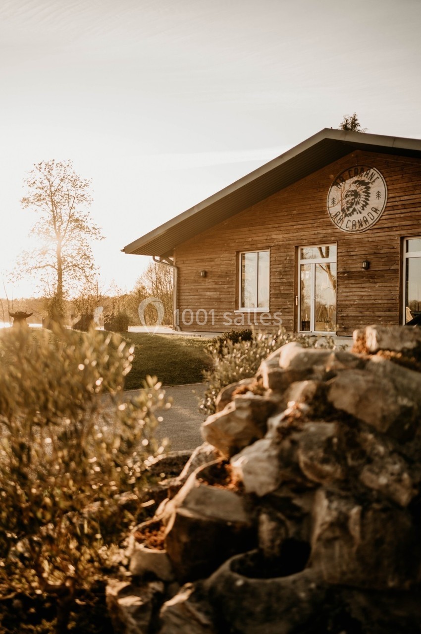 Bâtiment en bois avec un logo circulaire, entouré de végétation et éclairé par une lumière de coucher de soleil.