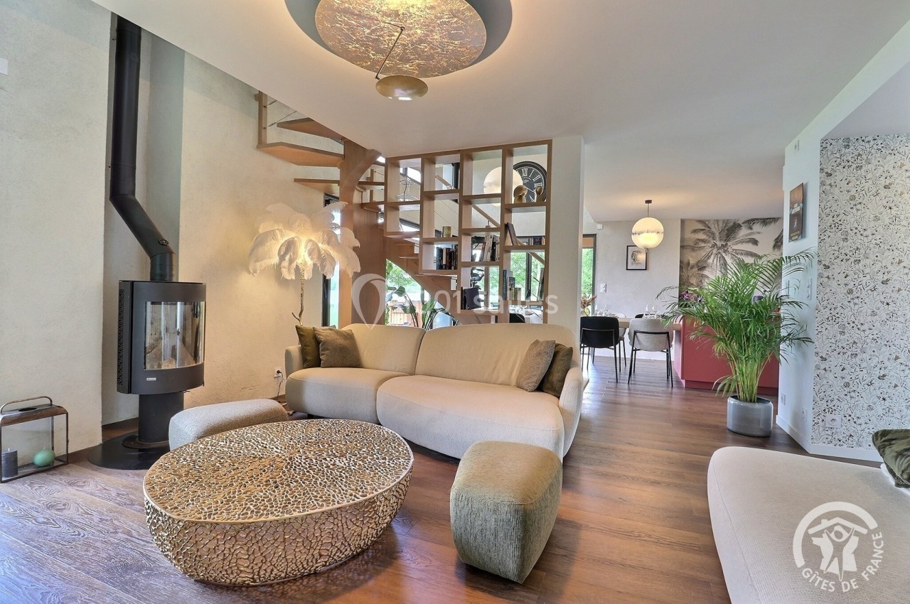 Salon moderne avec canapé beige, poêle à bois, table basse design et escalier en colimaçon en arrière-plan.