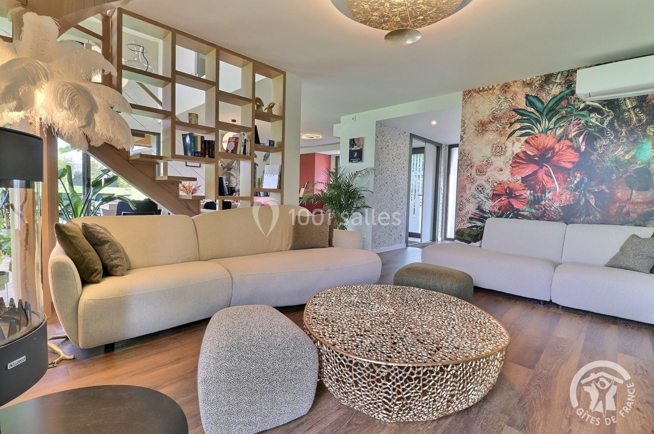 Salon moderne avec canapé beige, table basse en rotin, décoration murale florale et étagère en bois sous escalier.