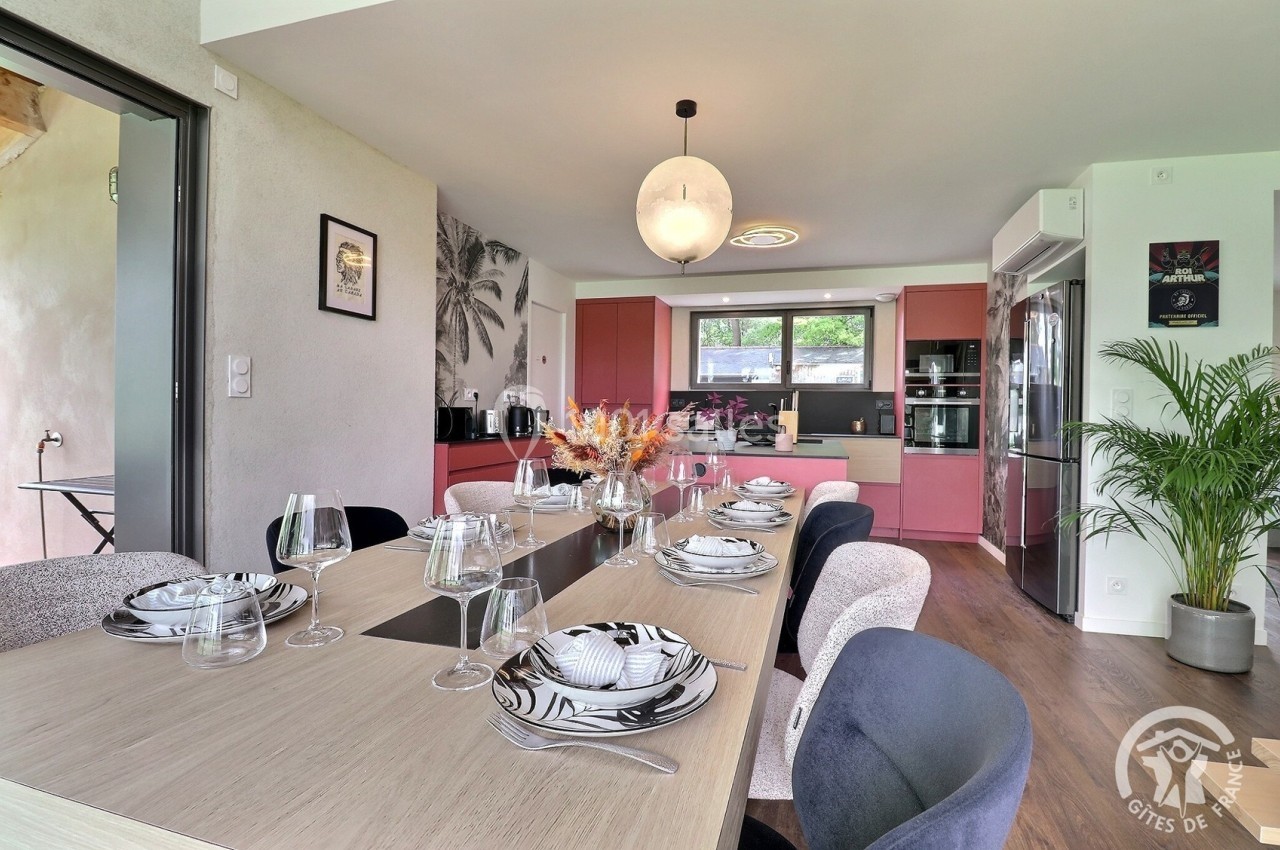 Salle à manger moderne avec table dressée, cuisine ouverte équipée en arrière-plan et décoration contemporaine.