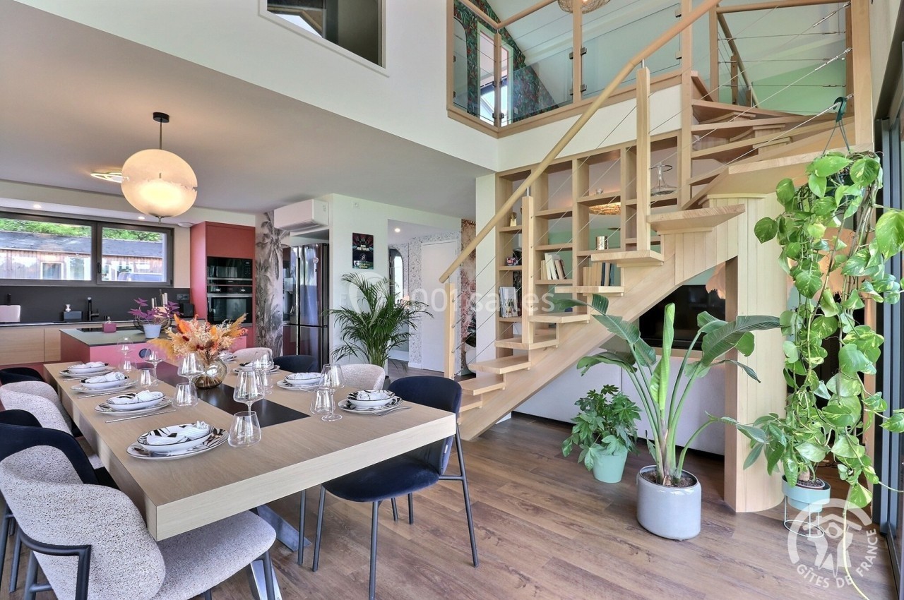 Salle à manger moderne avec table dressée, cuisine ouverte en arrière-plan et escalier en bois menant à l'étage.
