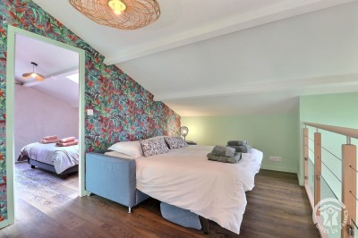 Chambre mansardée avec deux lits simples, murs en pierre apparente, lumière naturelle et décoration chaleureuse.