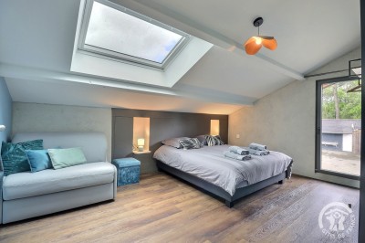 Chambre mansardée avec deux lits simples, murs en pierre apparente, lumière naturelle et décoration chaleureuse.