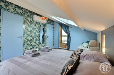 Chambre mansardée avec deux lits simples, murs en pierre apparente, lumière naturelle et décoration chaleureuse.