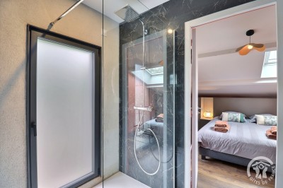 Chambre mansardée avec deux lits simples, murs en pierre apparente, lumière naturelle et décoration chaleureuse.