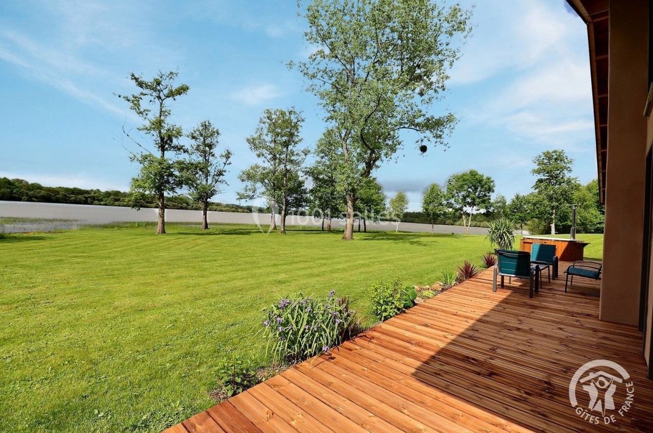 Terrasse en bois donnant sur un grand jardin verdoyant avec des arbres et un plan d'eau en arrière-plan.