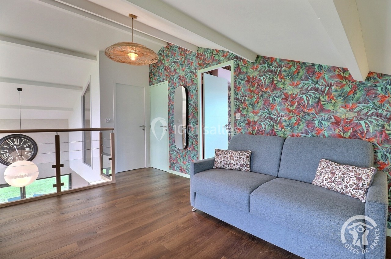 Canapé bleu dans un espace lumineux avec parquet, mur à motif tropical, et vue sur un escalier moderne.