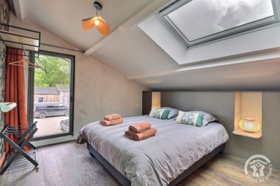 Chambre mansardée avec deux lits simples, murs en pierre apparente, lumière naturelle et décoration chaleureuse.