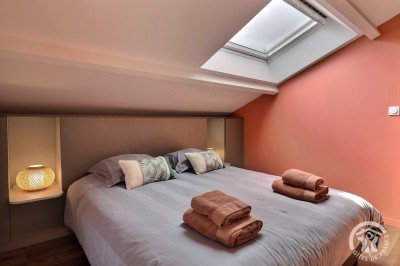 Chambre mansardée avec deux lits simples, murs en pierre apparente, lumière naturelle et décoration chaleureuse.