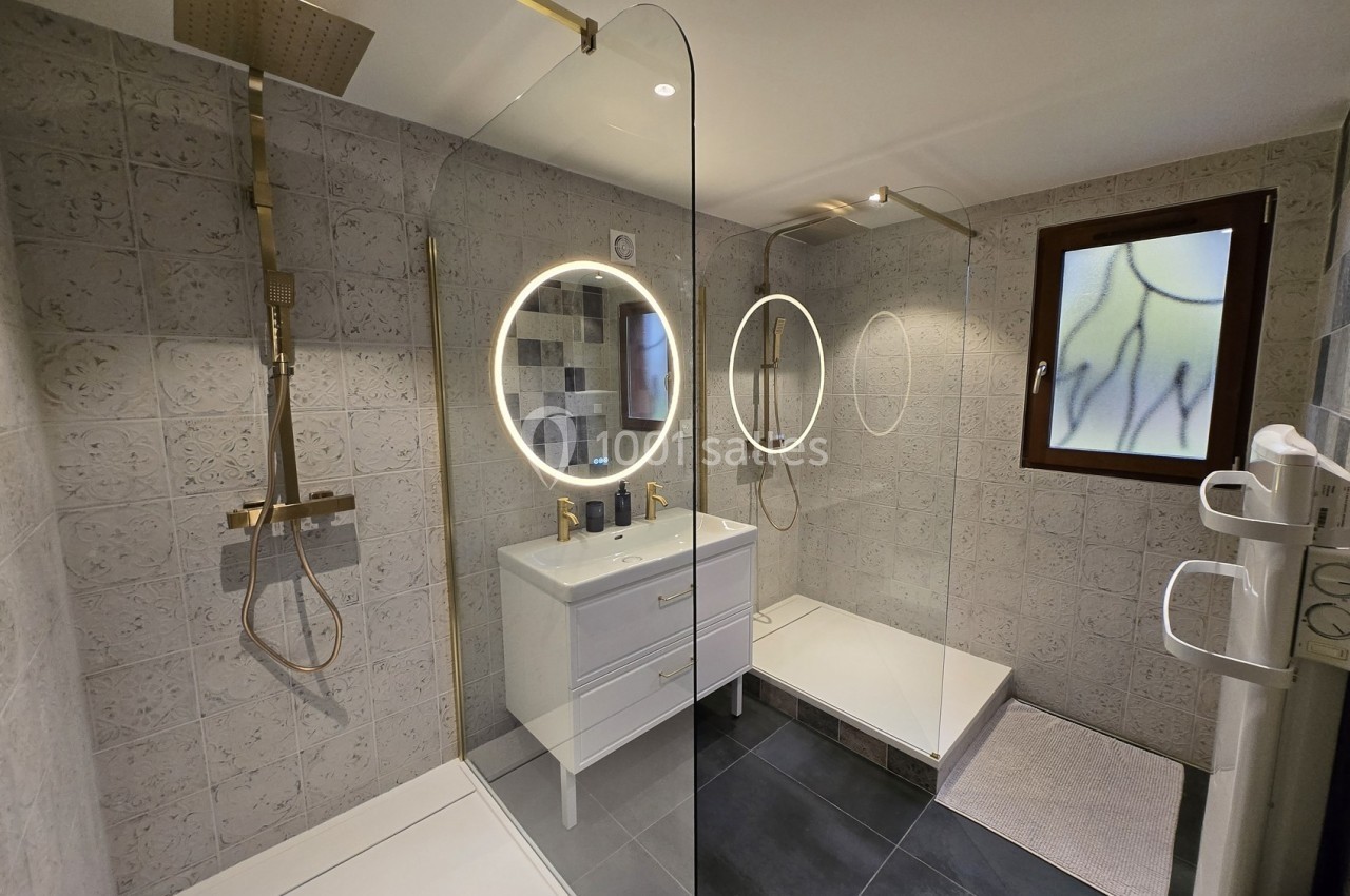 Salle de bain moderne avec douche à l'italienne, double vasque, miroirs ronds éclairés et carrelage texturé.