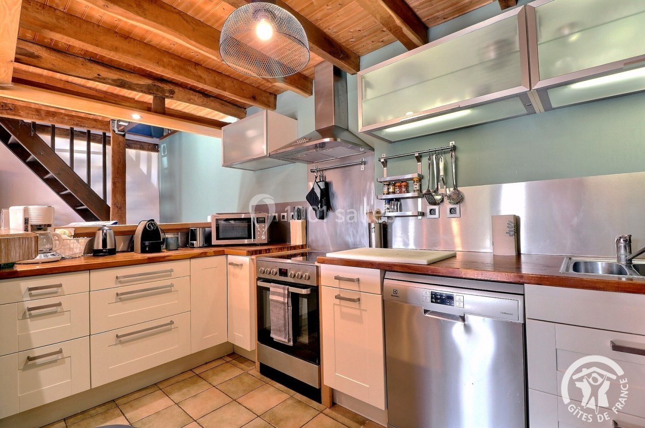 Cuisine moderne avec poutres apparentes, équipée d'appareils électroménagers, d'un plan de travail en bois et d'un évier en…