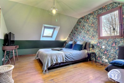 Chambre mansardée avec deux lits simples, murs en pierre apparente, lumière naturelle et décoration chaleureuse.