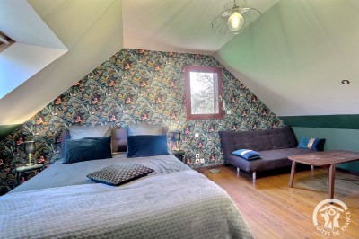 Chambre mansardée avec deux lits simples, murs en pierre apparente, lumière naturelle et décoration chaleureuse.