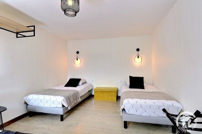Chambre mansardée avec deux lits simples, murs en pierre apparente, lumière naturelle et décoration chaleureuse.