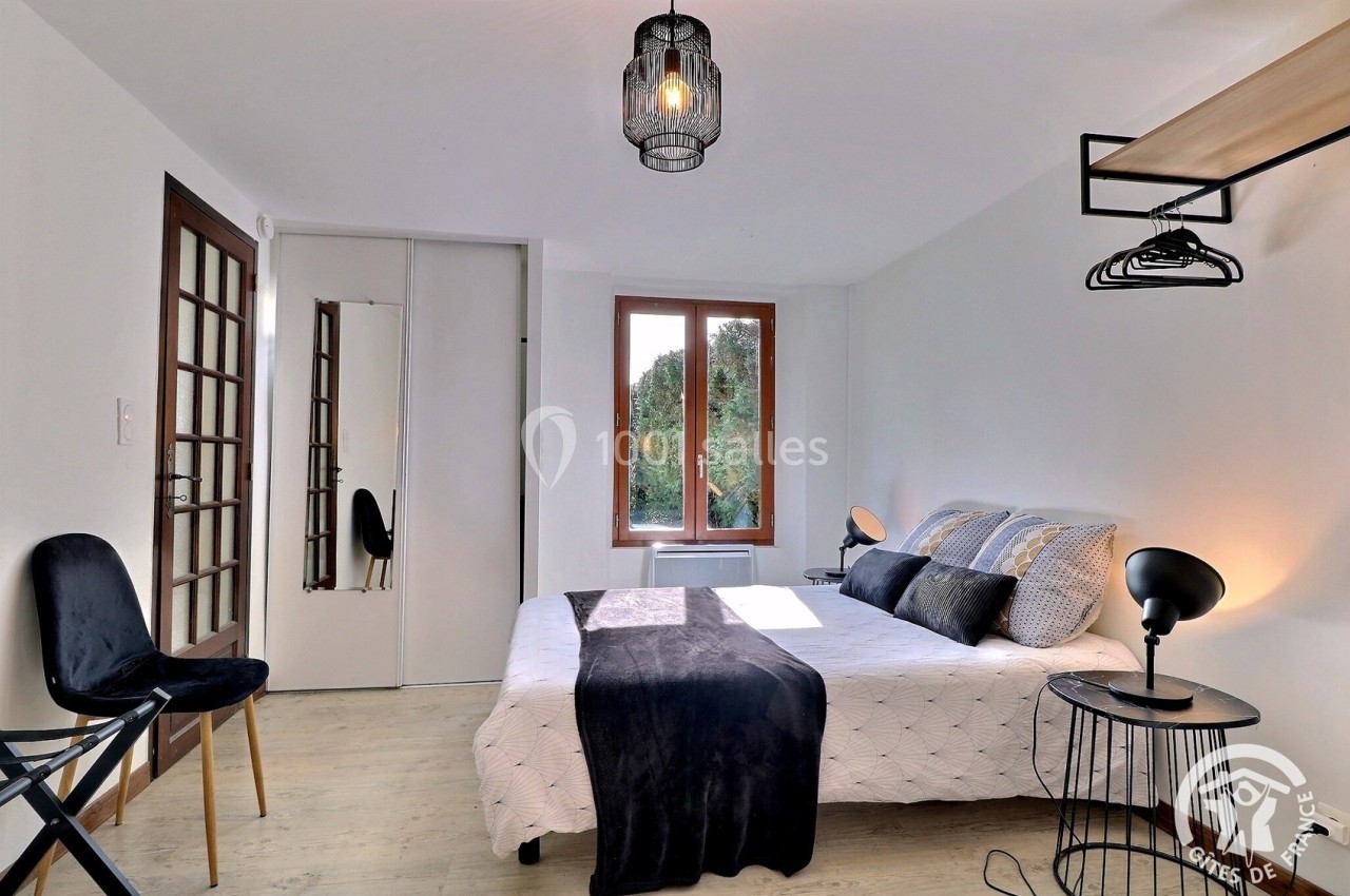 Chambre lumineuse avec lit double, mobilier moderne, miroir, et fenêtre donnant sur un espace arboré.