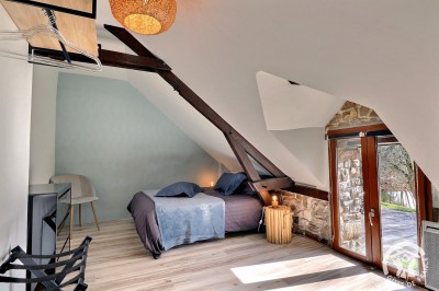 Chambre mansardée avec deux lits simples, murs en pierre apparente, lumière naturelle et décoration chaleureuse.
