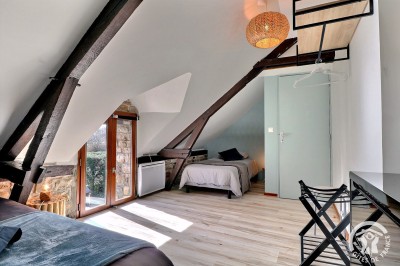 Chambre mansardée avec deux lits simples, murs en pierre apparente, lumière naturelle et décoration chaleureuse.