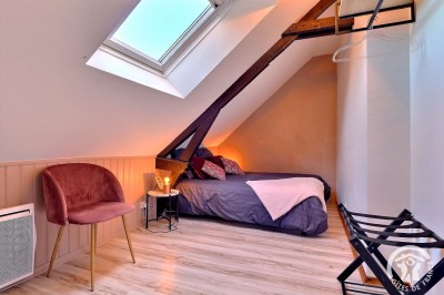 Chambre mansardée avec deux lits simples, murs en pierre apparente, lumière naturelle et décoration chaleureuse.