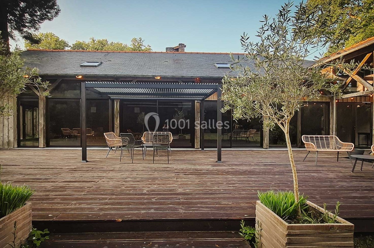 Terrasse en bois avec mobilier de jardin, pergola moderne et végétation environnante devant un bâtiment vitré.