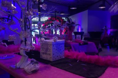 Salle décorée pour un anniversaire avec ballons noirs et dorés, tables dressées et une scène en fond.