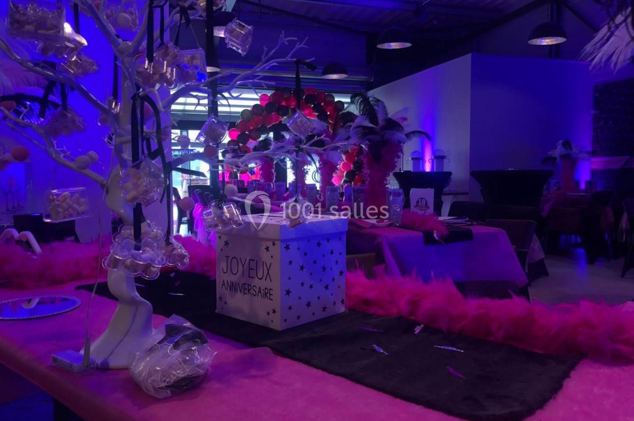 Salle décorée pour un anniversaire avec des tons roses et violets, des cadeaux et des éléments festifs sur les tables.