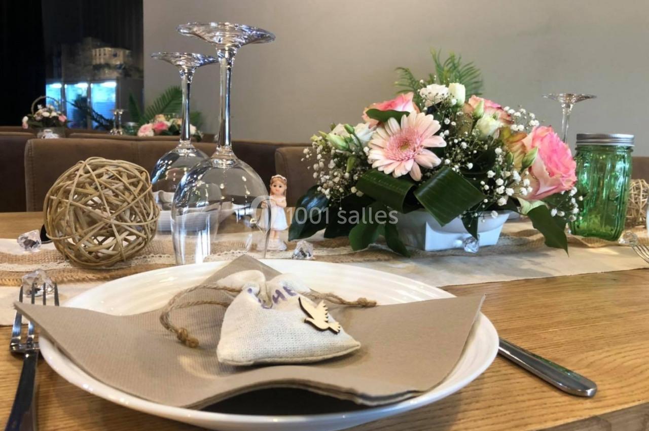 Table dressée avec une assiette, serviette beige, décoration florale, verres à pied et ornements en rotin.
