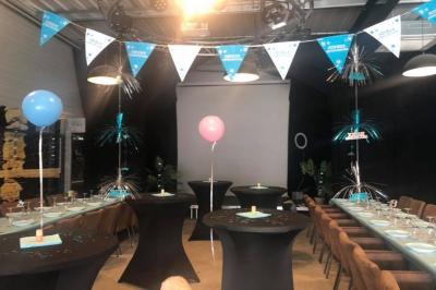 Salle décorée pour un anniversaire avec ballons noirs et dorés, tables dressées et une scène en fond.