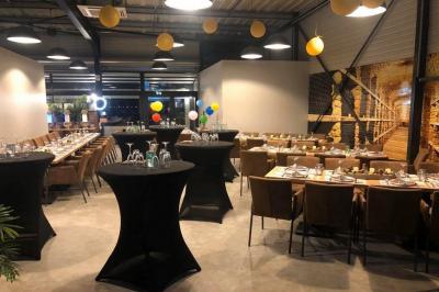 Salle décorée pour un anniversaire avec ballons noirs et dorés, tables dressées et une scène en fond.