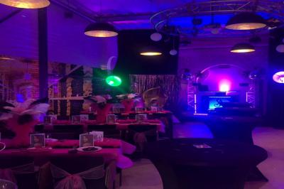 Salle décorée pour un anniversaire avec ballons noirs et dorés, tables dressées et une scène en fond.