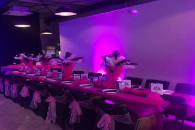 Salle décorée pour un anniversaire avec ballons noirs et dorés, tables dressées et une scène en fond.