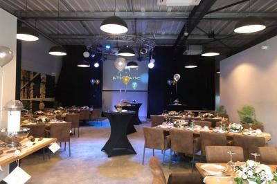 Salle décorée pour un anniversaire avec ballons noirs et dorés, tables dressées et une scène en fond.