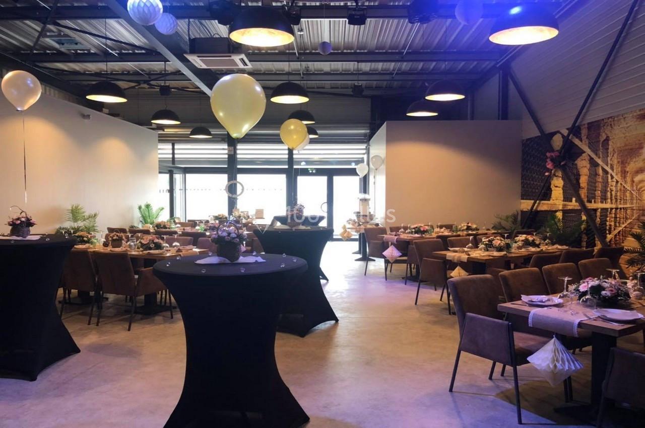 Salle décorée pour un événement avec tables dressées, ballons suspendus et éclairage chaleureux.