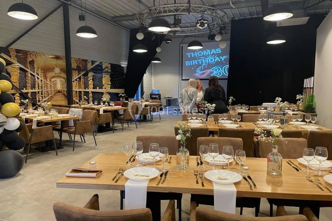 Salle décorée pour un anniversaire avec tables dressées, ballons noirs et dorés, et écran affichant ’Thomas Birthday 30’.