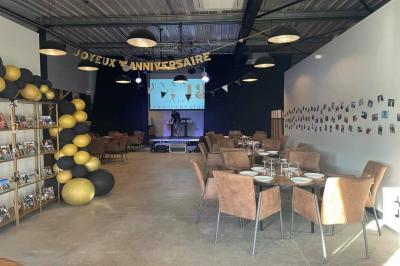 Salle décorée pour un anniversaire avec ballons noirs et dorés, tables dressées et une scène en fond.