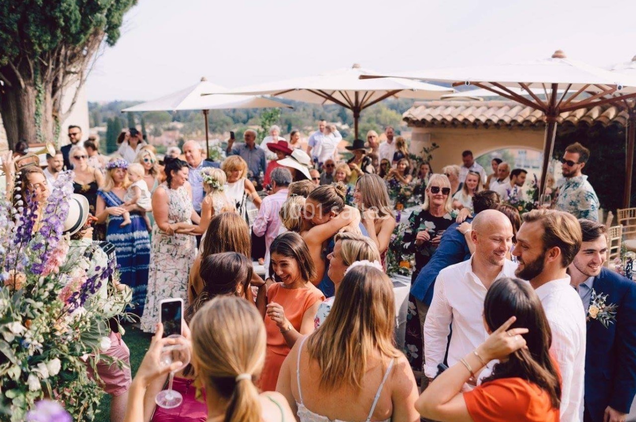 Groupe de personnes réunies en extérieur lors d'un événement festif, entourées de parasols et de végétation.