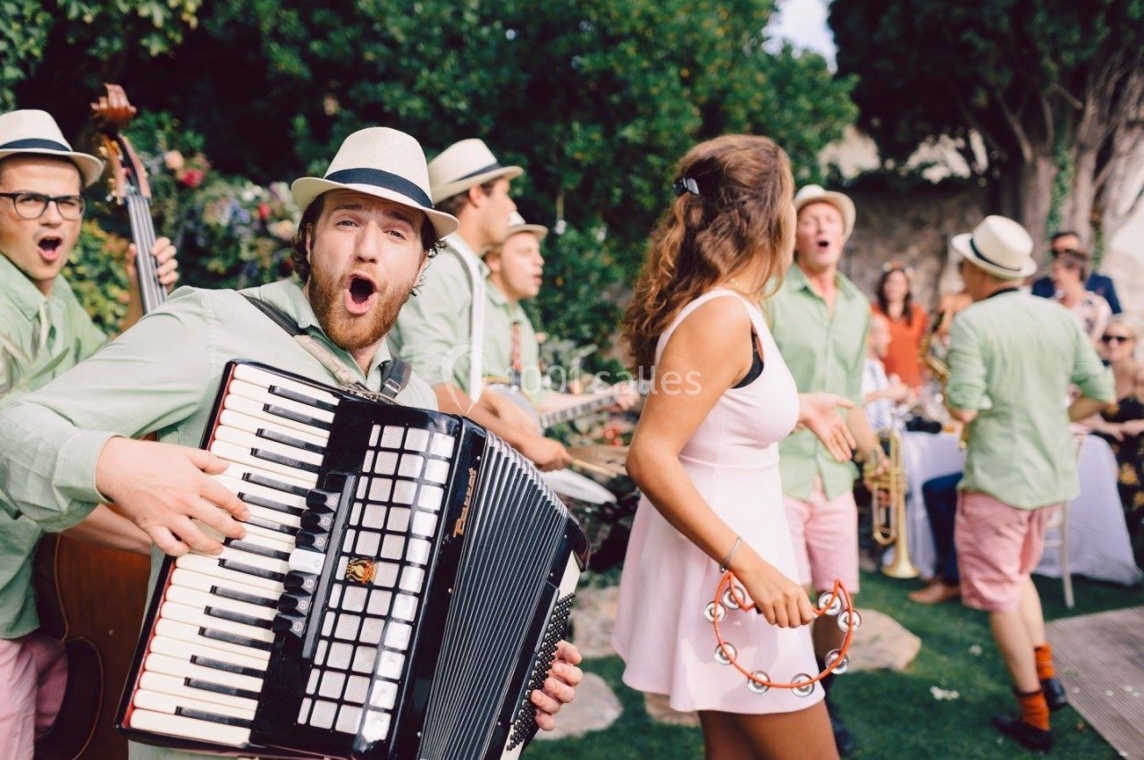 Un groupe de musiciens en plein air joue des instruments tandis qu'une femme danse avec un tambourin.