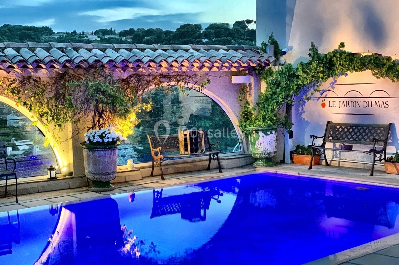 Piscine éclairée en soirée, entourée de bancs, plantes grimpantes et décorations méditerranéennes.