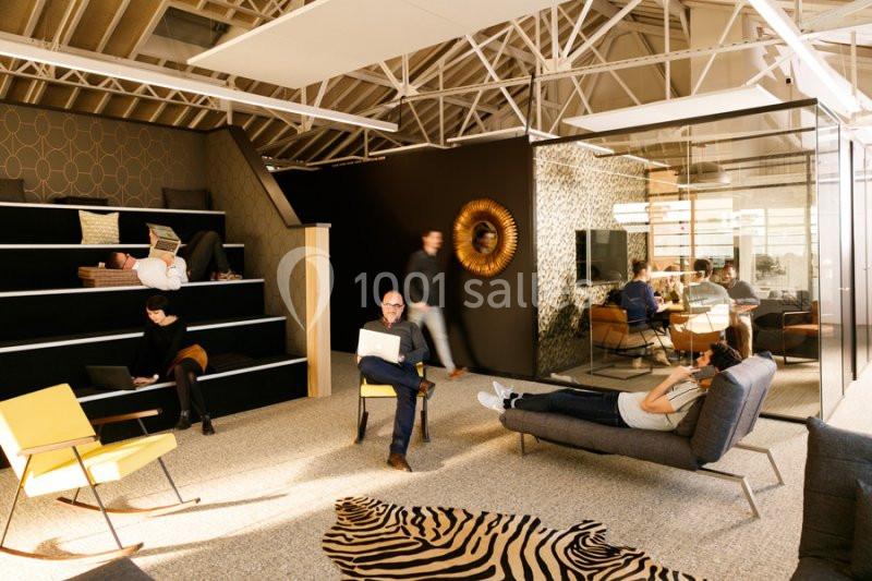 Espace de travail moderne avec fauteuils, tables, tapis zébré et plusieurs personnes travaillant ou discutant.