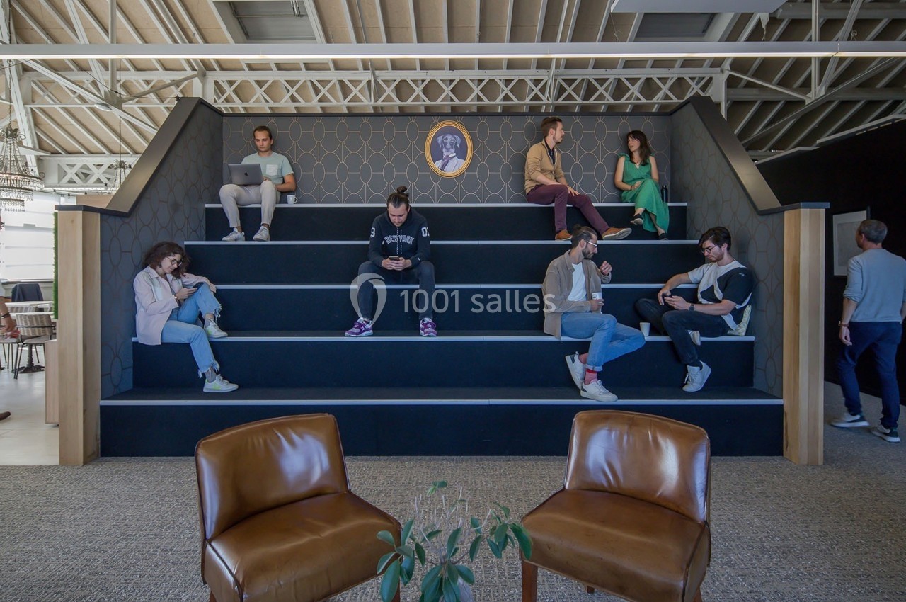 Des personnes assises sur des gradins dans un espace de travail moderne, certaines utilisant des ordinateurs ou des…