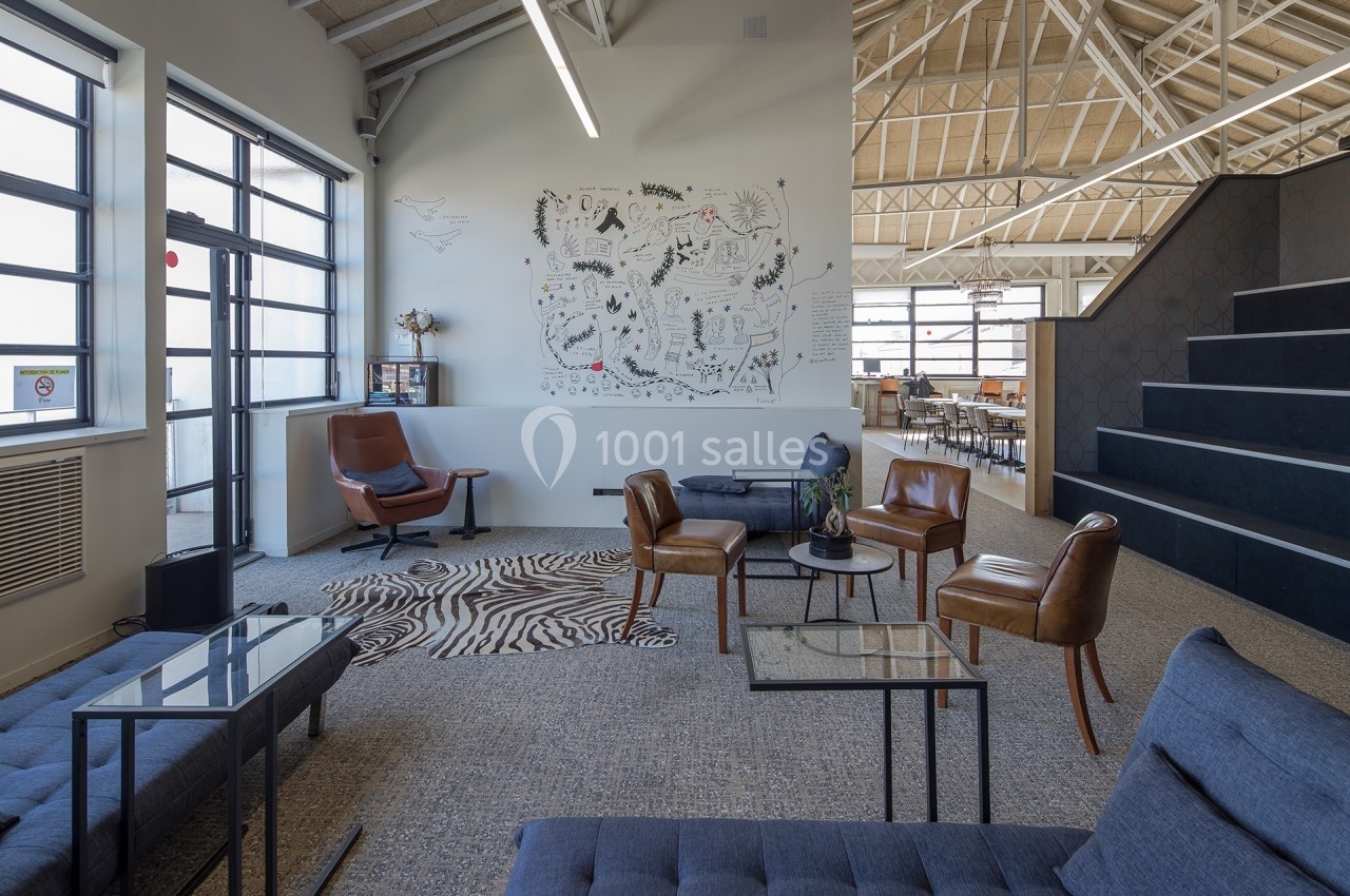 Espace de coworking lumineux avec fauteuils, tables basses, tapis zébré et mur décoré de dessins.