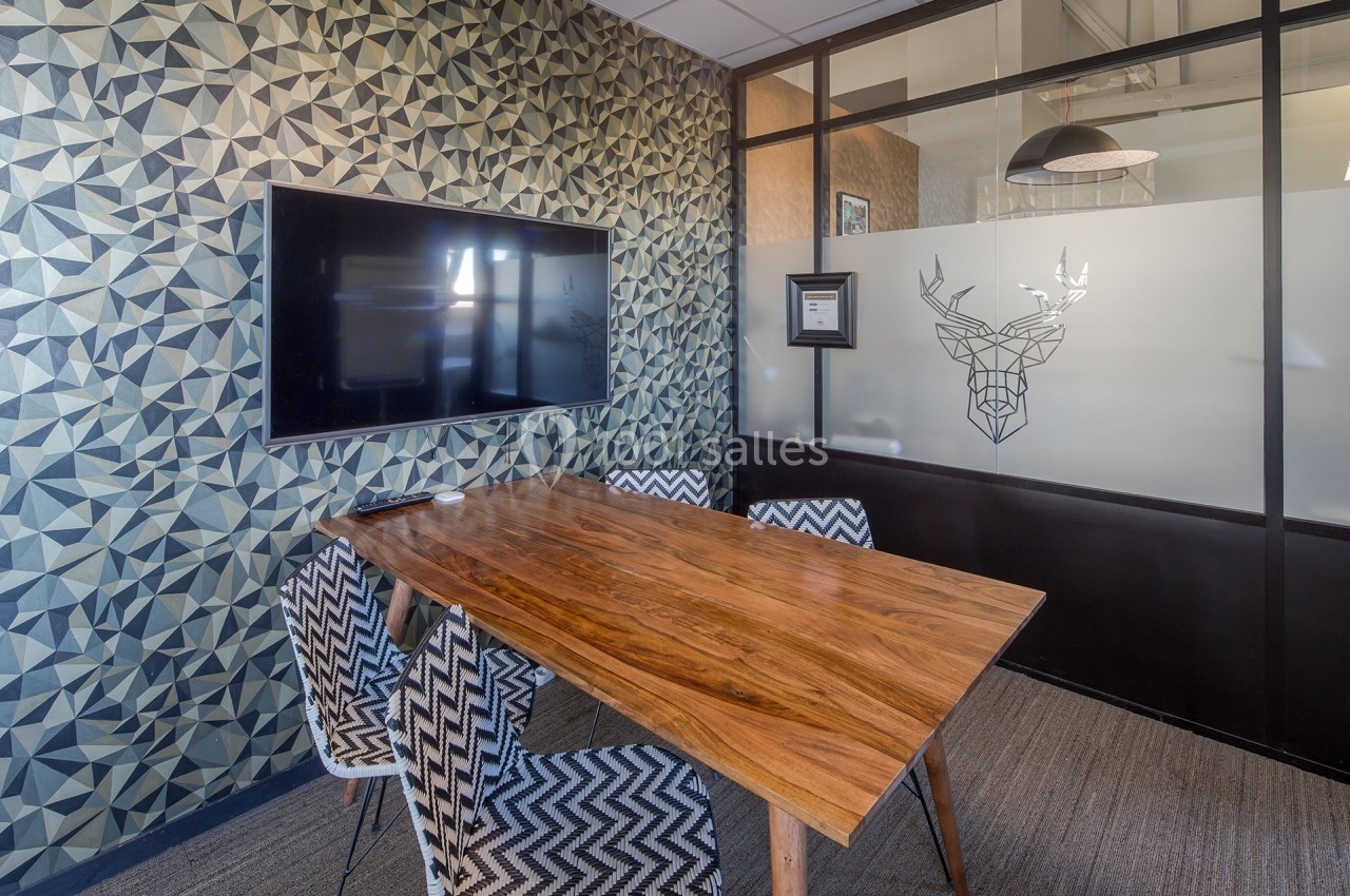Salle de réunion moderne avec table en bois, chaises à motifs géométriques et écran mural.