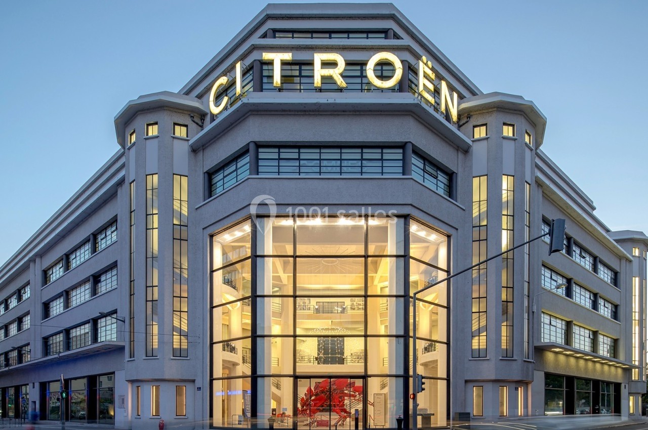 Bâtiment moderne avec façade vitrée et enseigne lumineuse ’Citroën’, éclairé en fin de journée.